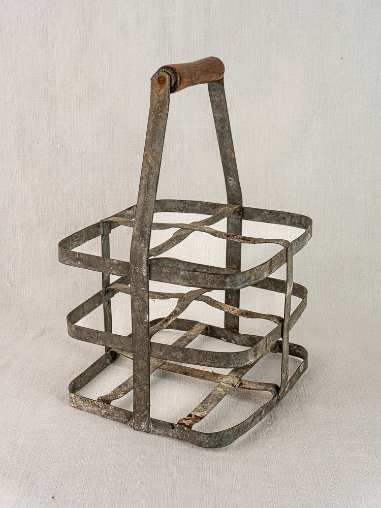 Antique French zinc and wood wine carrier with four bottle spaces and wooden handle on light fabric.