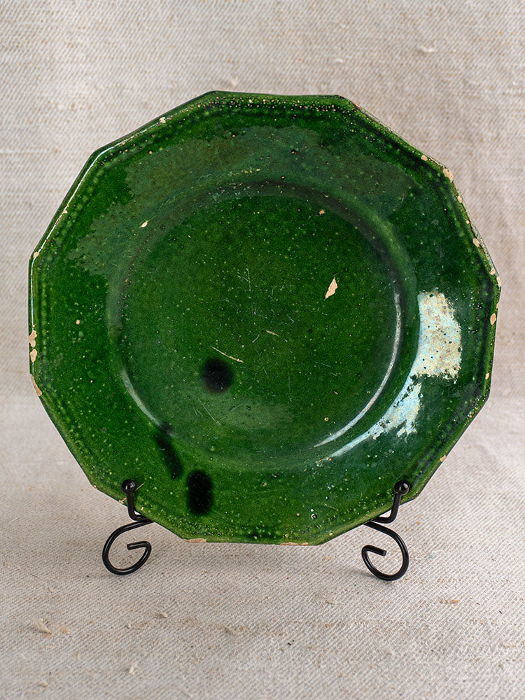 Antique French green glazed plates from Drôme with worn edges, dark spots, on black metal stand and textured beige fabric.
