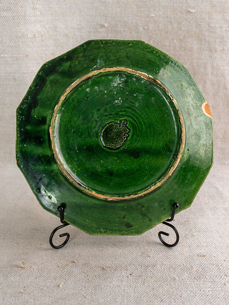 Pair of antique French green glazed octagonal plates, worn edges, on black stand with beige fabric backdrop.