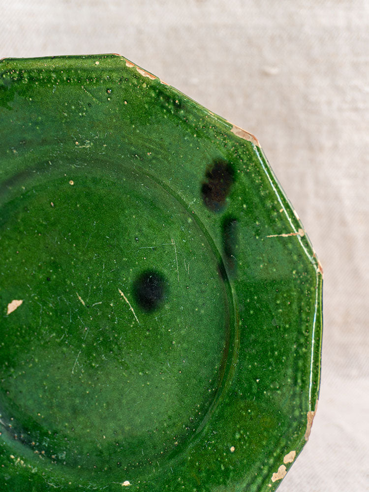 Pair of antique French green glazed plates with worn, chipped edges and dark spots on beige textured fabric.