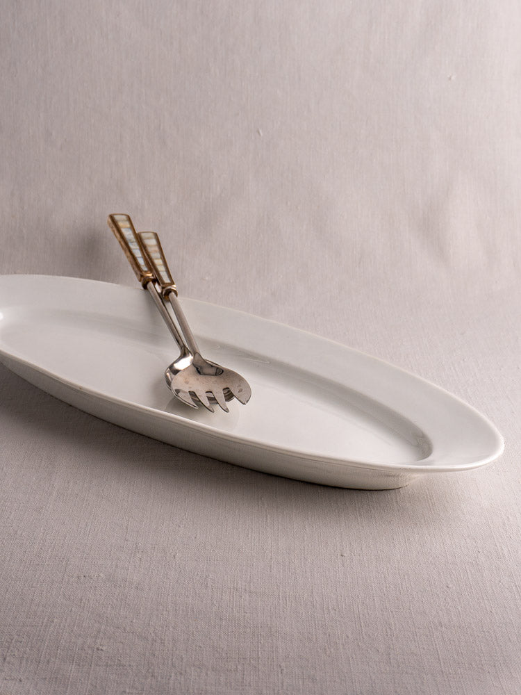 19th-century French white ironstone fish platter with metal pasta server on light gray fabric.