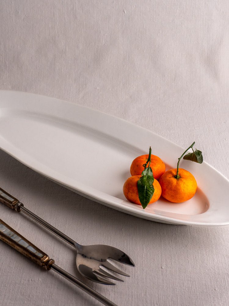Antique French 19th-century white ironstone fish platter with oranges, serving fork, and spoon on fabric.