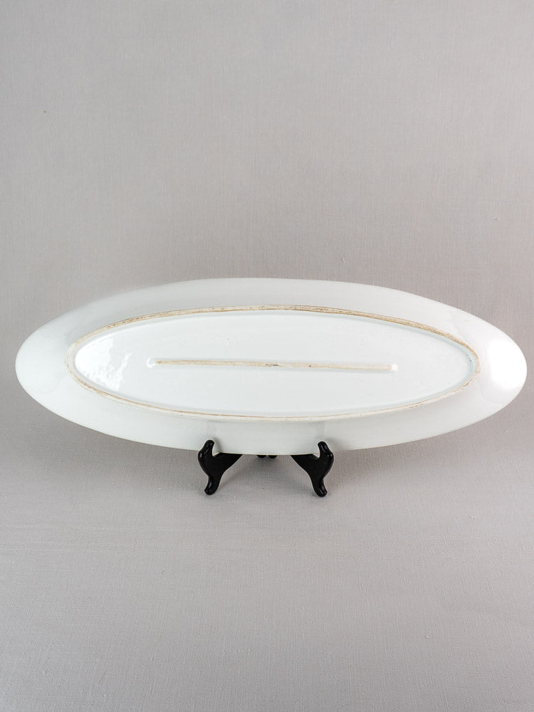 19th-century white ironstone French fish platter with gold trim on black stand, light gray background.