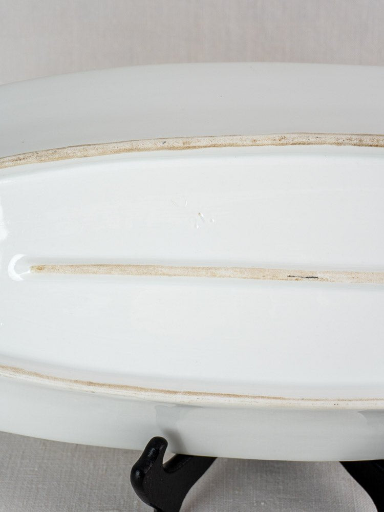 Underside of antique French 19th-century white ironstone fish platter with unglazed strips, on black stand.