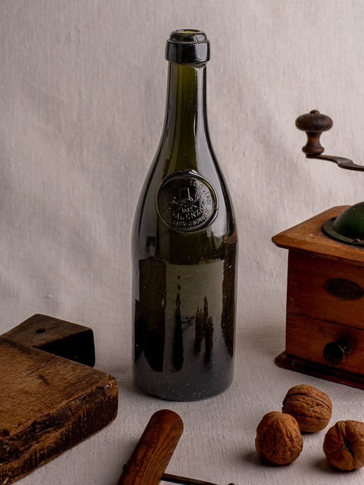 Hand blown dark green Italian wine bottle with black wax seal and embossed emblem on gray surface.