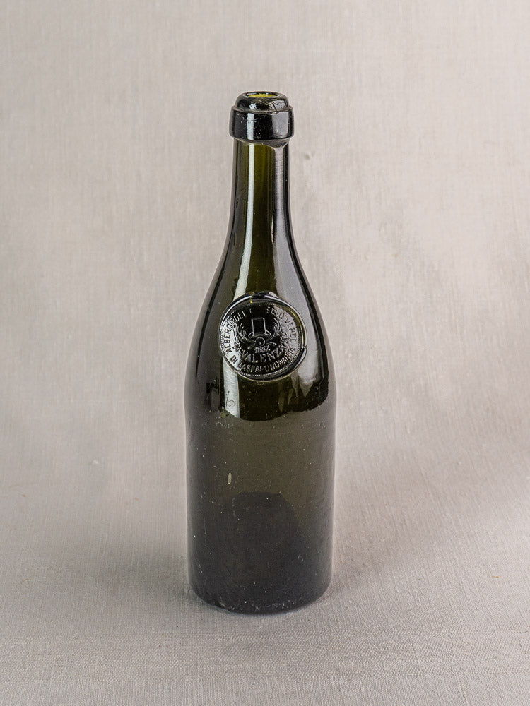 Hand blown dark green Italian wine bottle with black wax seal and embossed emblem on gray surface.