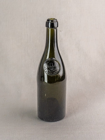 Hand blown dark green Italian wine bottle with black wax seal and embossed emblem on gray surface.