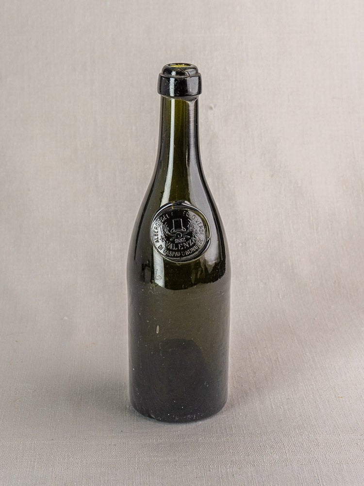 Hand blown dark green Italian wine bottle with black wax seal and embossed emblem on gray surface.