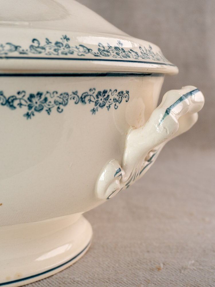 Antique French Longwy ironstone soup tureen with Capucine blue transferware rim and white handle on fabric backdrop.