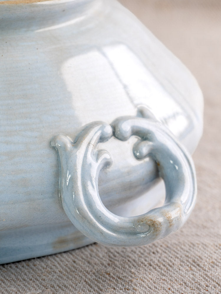 Antique Villeroy & Boch Mettlach tureen with soft blue glaze and curved handle on beige textured surface.