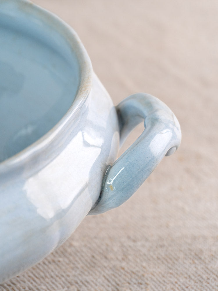 Antique Mettlach Villeroy and Boch tureen with soft blue glaze and curved handle on beige fabric.
