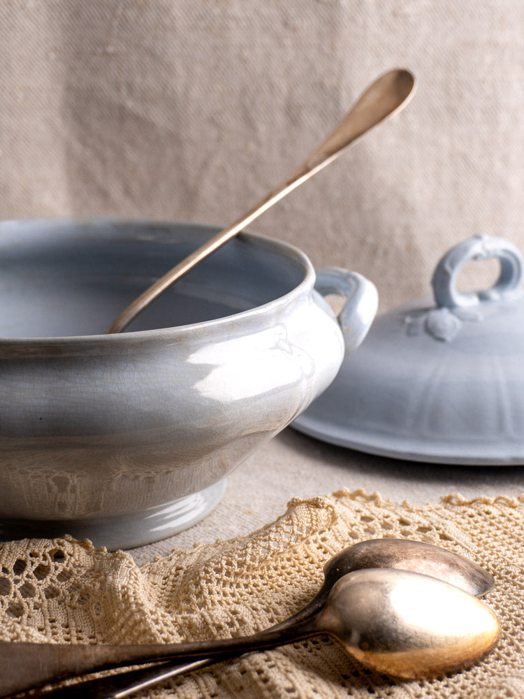 Antique Villeroy and Boch Mettlach tureen with soft blue glaze, lid, ladle, and vintage spoons on crocheted lace.