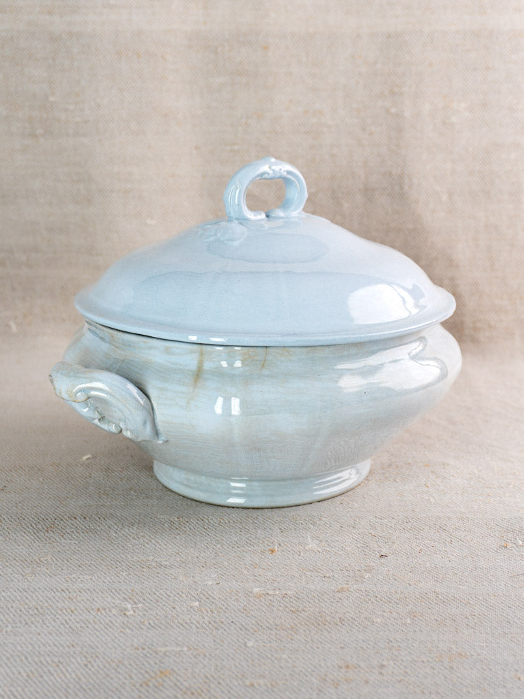 Antique Mettlach tureen by Villeroy and Boch with soft blue glaze, ornate handles, on tan fabric.