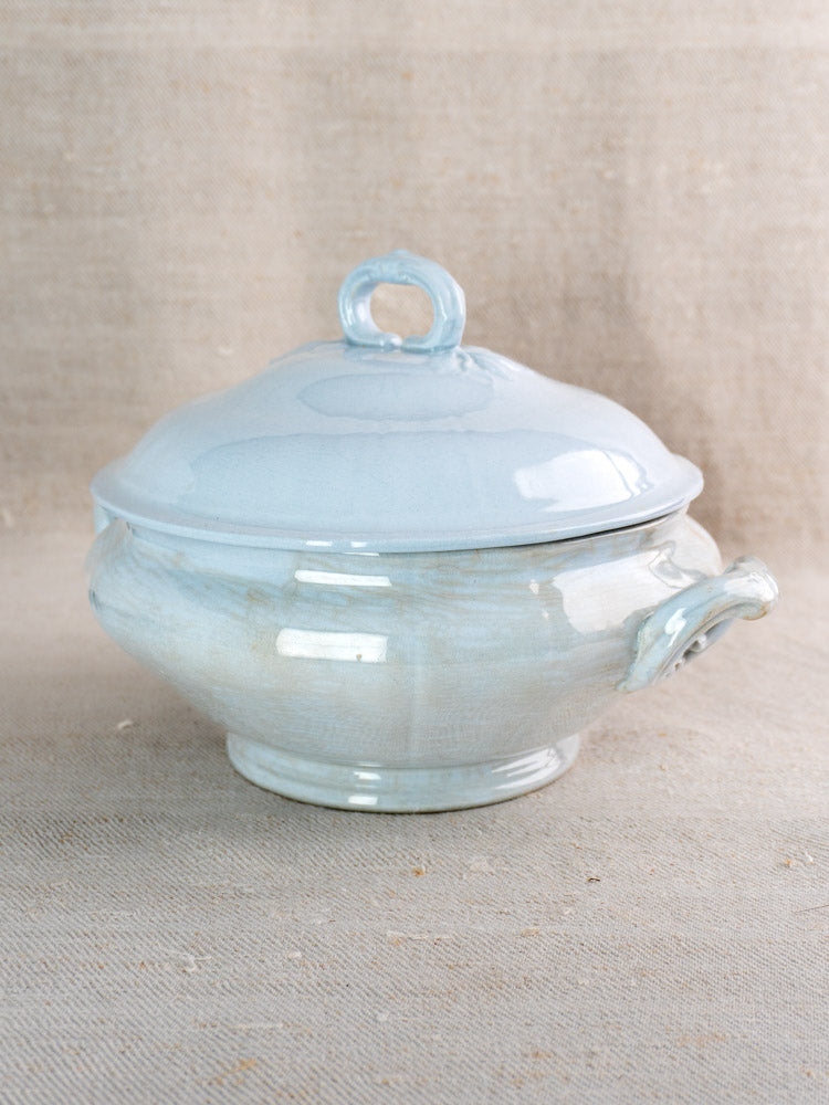 Antique Villeroy and Boch Mettlach tureen with soft blue glaze, matching lid and handles, on beige fabric.