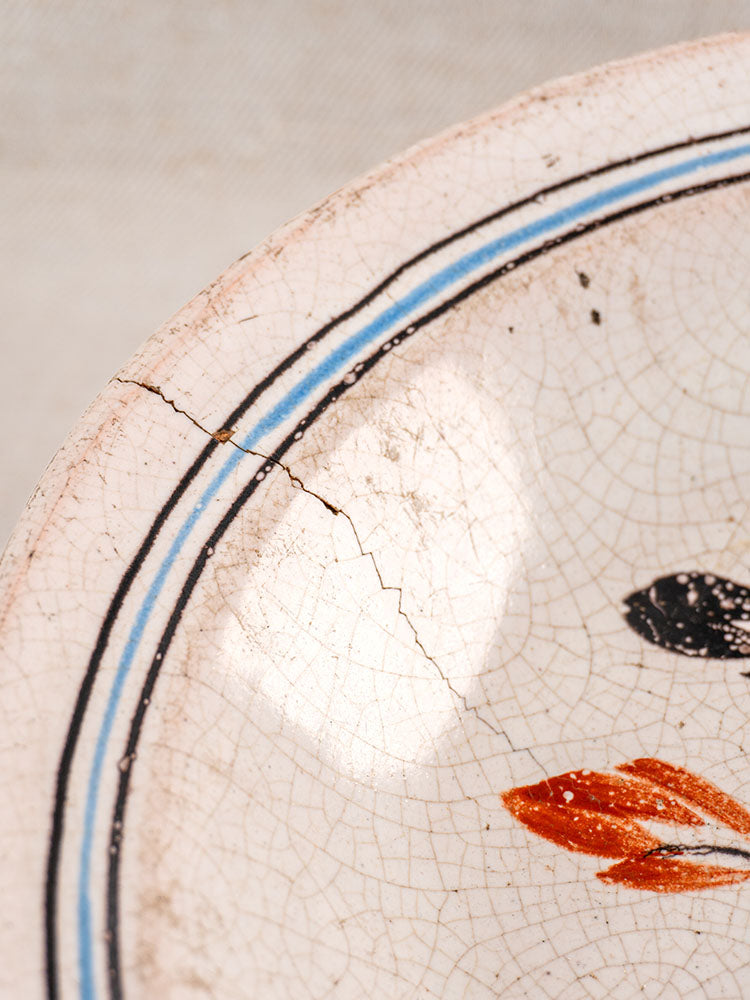 Antique French faience plate with blue and black border, orange design, glaze crazing, and rim-to-center crack.