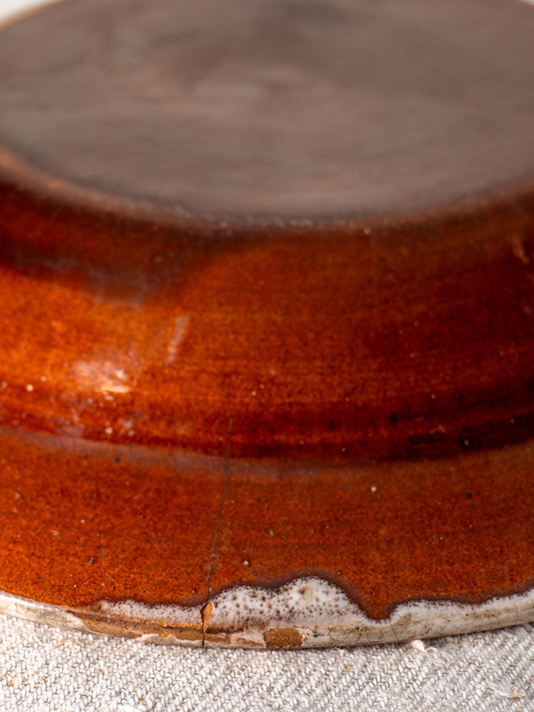 Antique French faience plate with glossy reddish-brown glaze and unglazed rim on textured fabric.