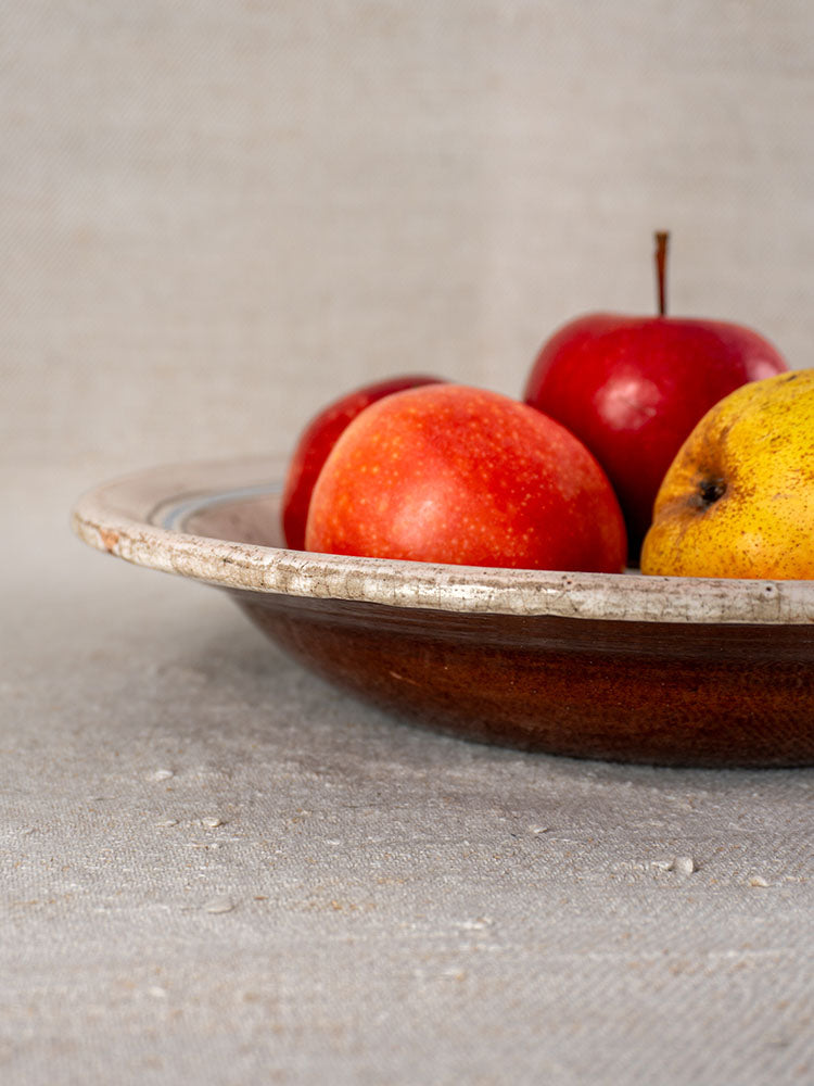 Antique French faience plate from Forges-les-Eaux with apples, pear, and peach on textured fabric background.