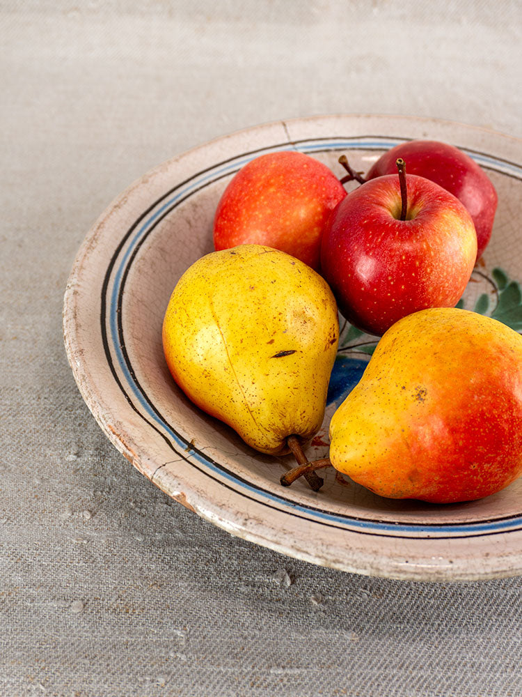 Antique French faience Cul Noir plate with two yellow pears and two red apples on beige textured surface.