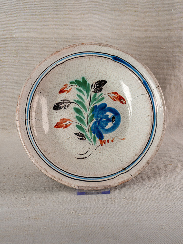 19th century Forges-les-Eaux French faience plate, blue floral center, double blue border, visible cracks, on neutral fabric.
