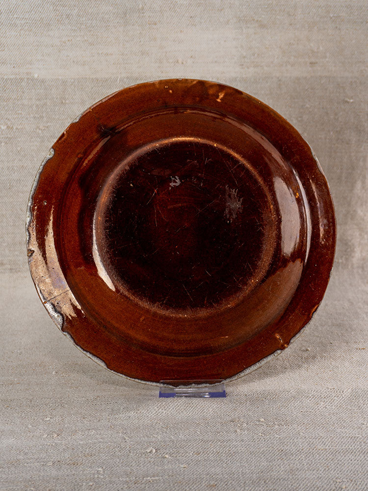 19th-century French faience plate with glossy dark brown glaze, gently worn edges; upright on neutral textured surface.