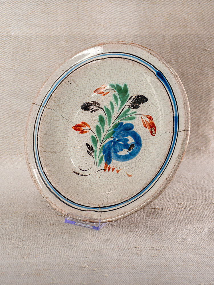 19th century French faience plate with crackled glaze, hand-painted floral design, on clear stand and beige background.