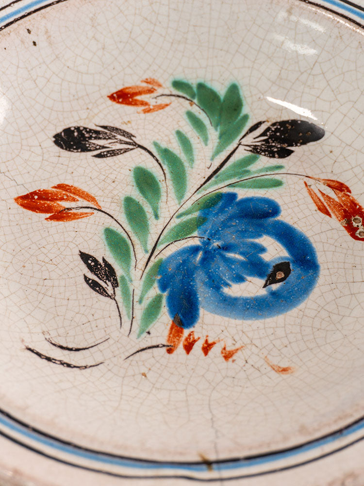 Antique French faience plate with hand-painted floral motifs, glaze crackling, and blue concentric rim lines.