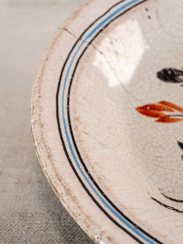 Antique French faience plate from Forges-les-Eaux with blue and black border, red detailing, and aged surface cracks.