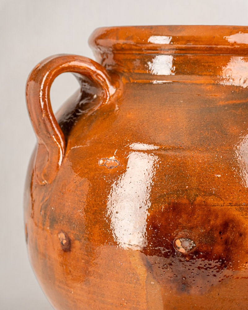 Antique French Provençal terracotta oil jar with brown glazed surface, curved handle, and textured finish.