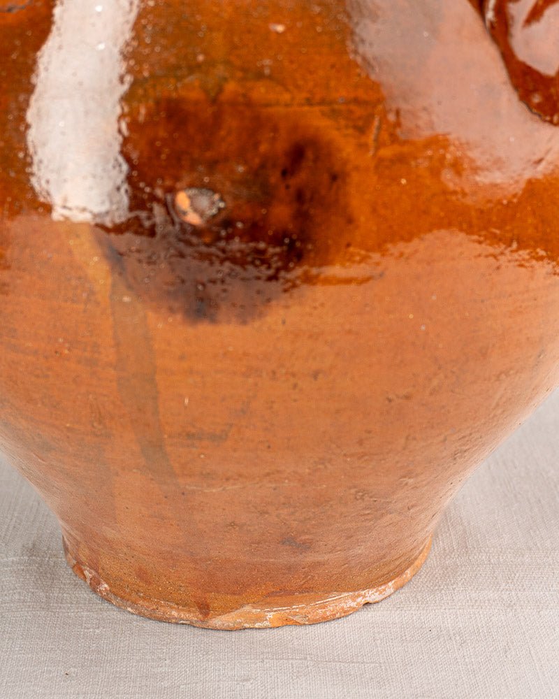 Lower section of antique French Provencal terracotta oil jar with warm brown glaze, on light fabric.
