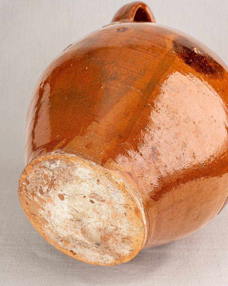 Antique French oil jar in glazed brown terracotta with textured surface and worn unglazed base.