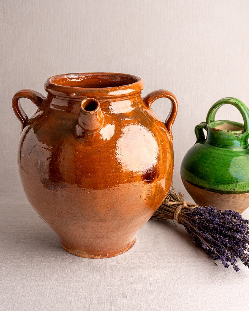 Large 19th-century French glazed terracotta oil jar with three handles, near a green jug and dried lavender.