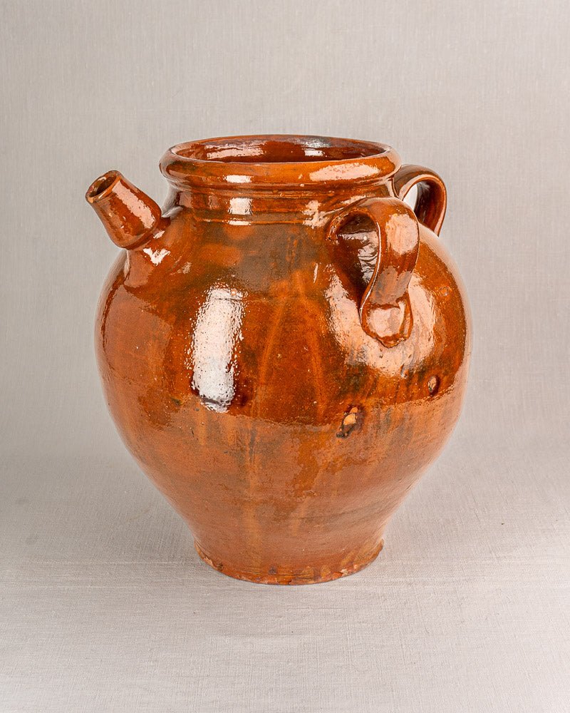 Antique French oil jar in glossy brown Provencal glazed terracotta with two handles, on gray surface.