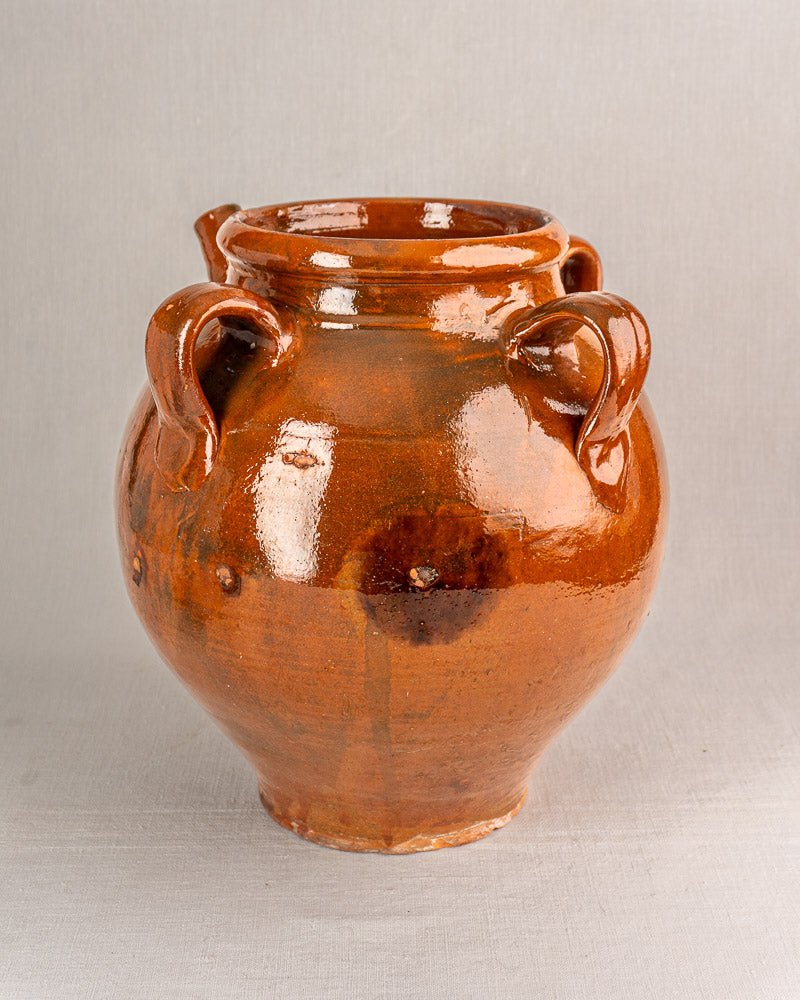 Antique 19th-century French terracotta oil jar with four handles and brown glaze on gray surface.