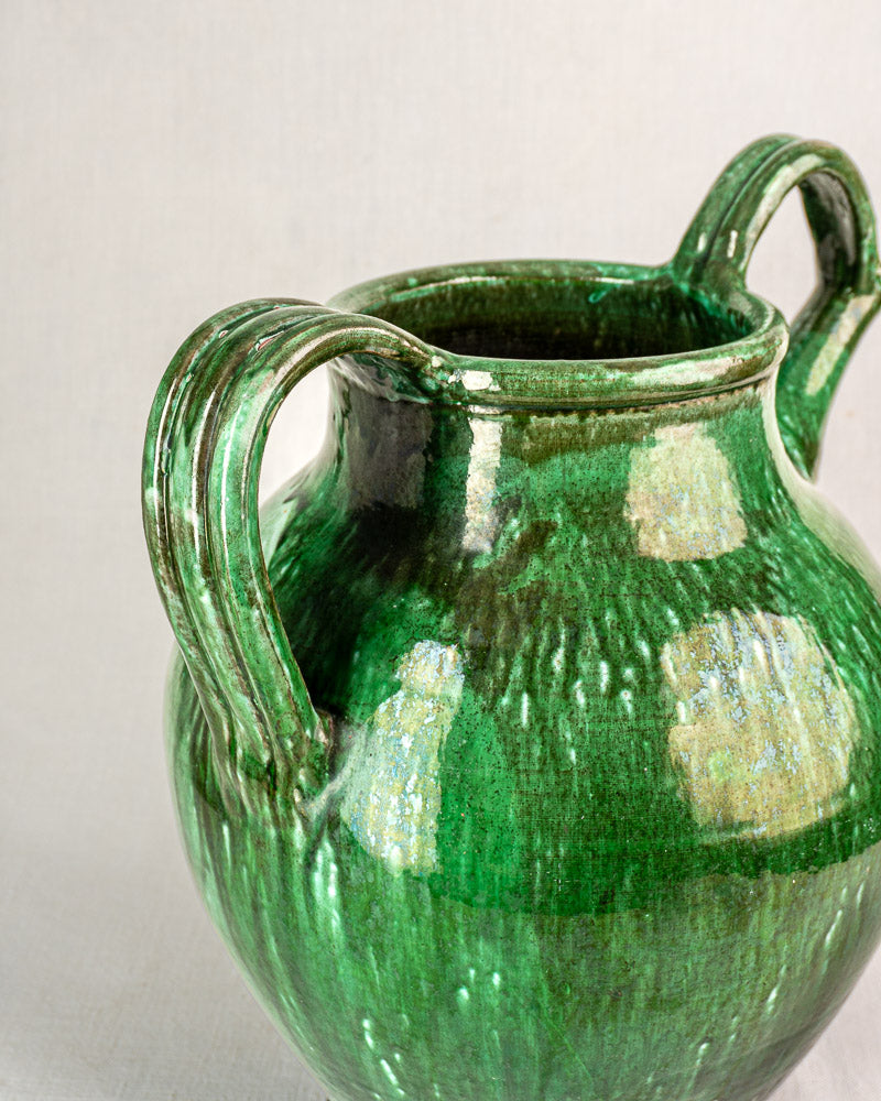 19th-century French green glazed earthenware cruche with two handles, inspired by traditional water jugs, set on a plain background.