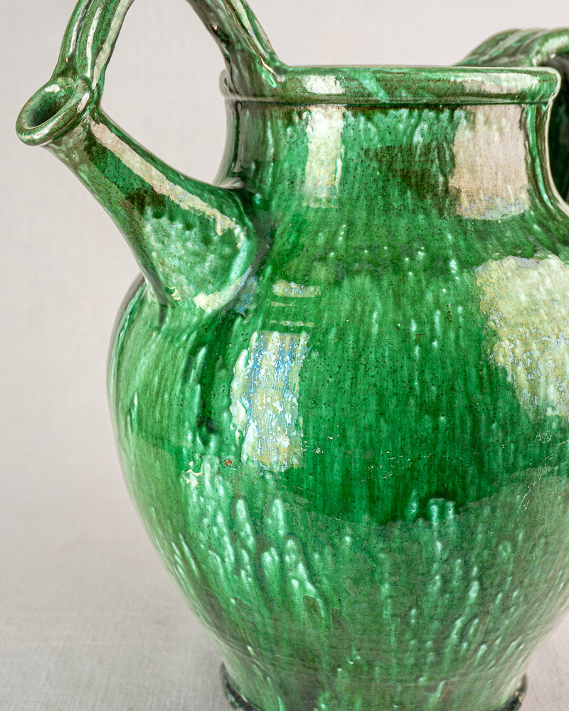Antique French green-glazed earthenware cruche with two curved handles, spout, and textured glossy surface.