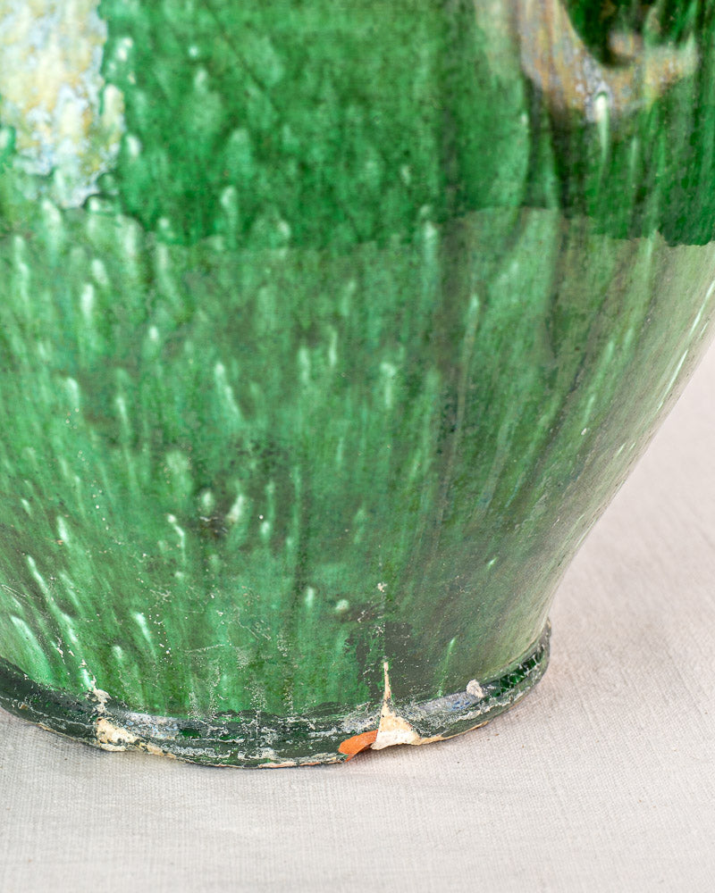 Base detail of 19th-century French green glazed earthenware cruche with worn, textured surface on pale background.