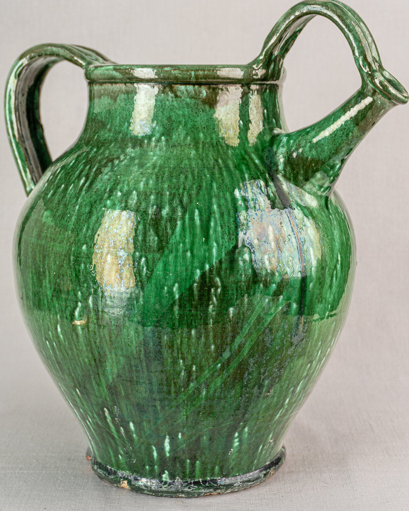 19th-century French green glazed earthenware cruche with two handles, spout, and rounded body on neutral surface.