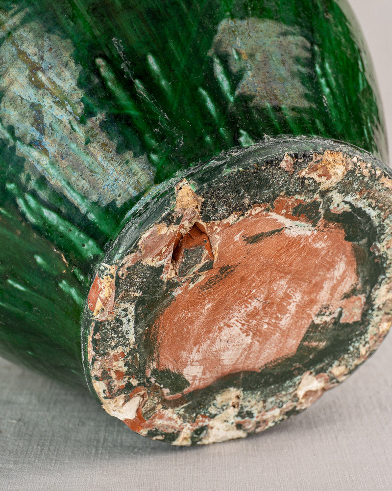 Detail of antique French cruche base, green glazed earthenware with weathered edges, reddish clay, worn glaze, and chipping.