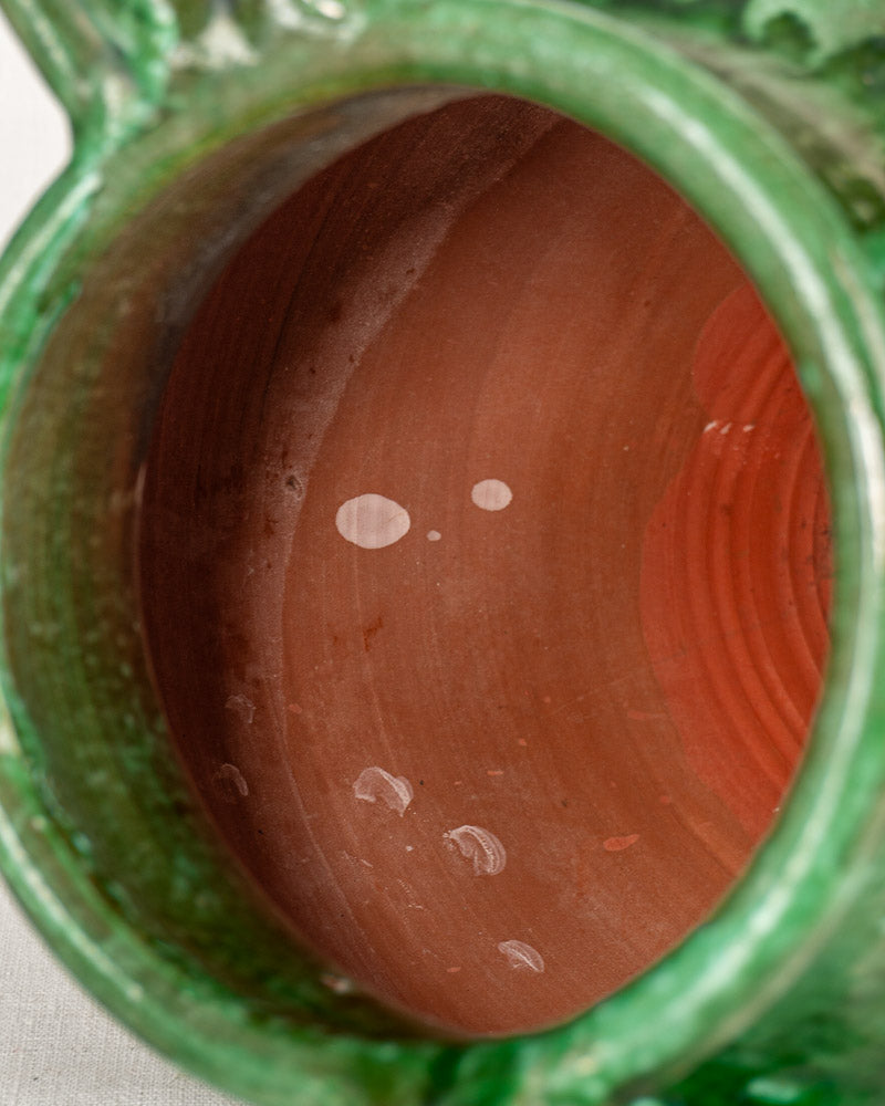 Reddish-brown interior of antique French cruche with white spots and green-glazed earthenware surface.