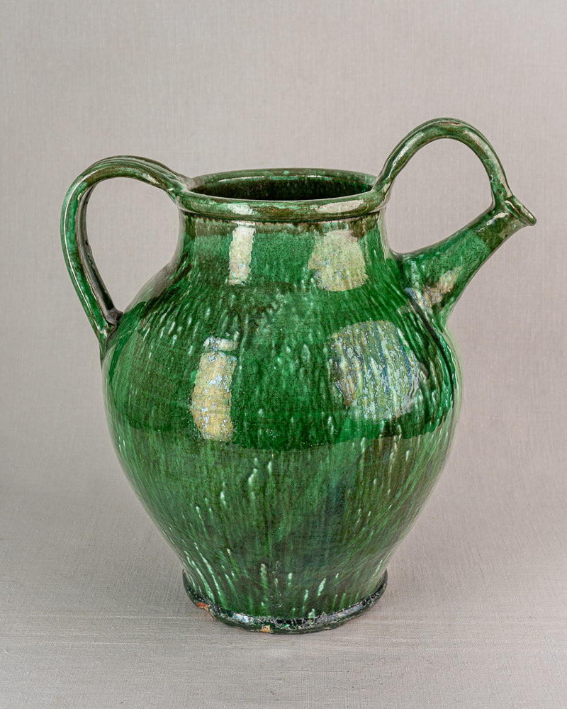 19th-century French green glazed earthenware cruche with two handles and spout on neutral surface.