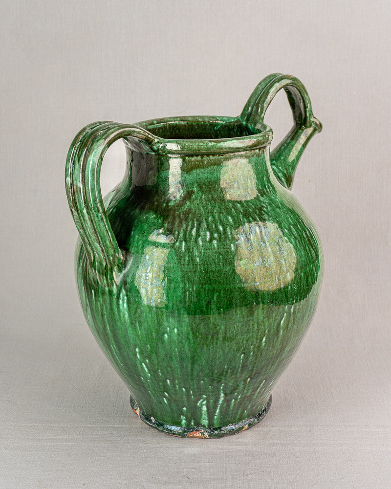 19th-century French green glazed earthenware cruche with curved handles and glossy, textured surface on light background.