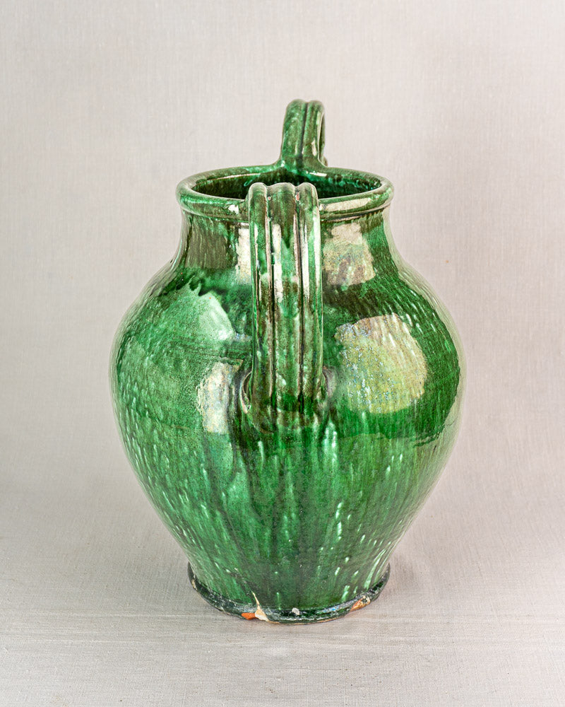 19th-century French green glazed earthenware cruche jug with dual vertical handles, wide body, and narrow neck on gray backdrop.