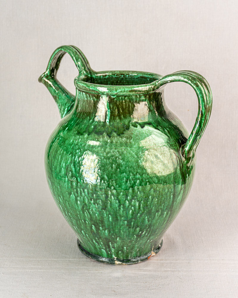 19th-century French green glazed earthenware cruche with two handles, wide spout, and rounded body on light background.