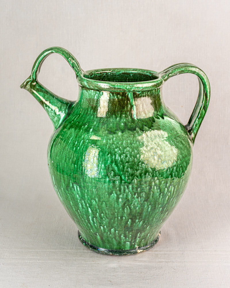 19th-century French green glazed earthenware cruche with wide body, two handles, and spout on light background.