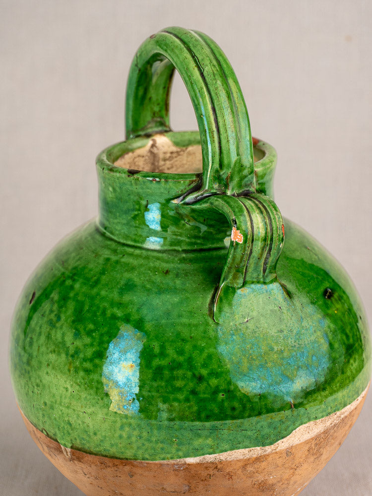 Antique French green glazed terracotta gargoulette with rounded body and arched handle, slight clay chips, on neutral background.