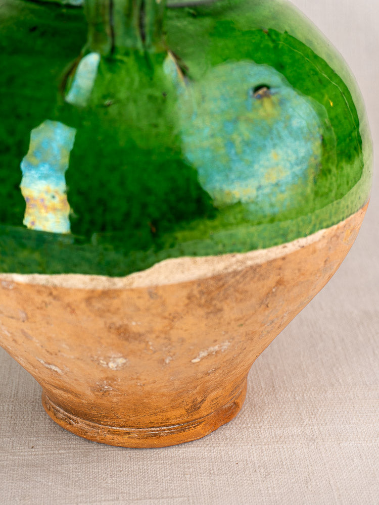 Antique French gargoulette cruche with green glazed terracotta and unglazed tan base on neutral fabric background.