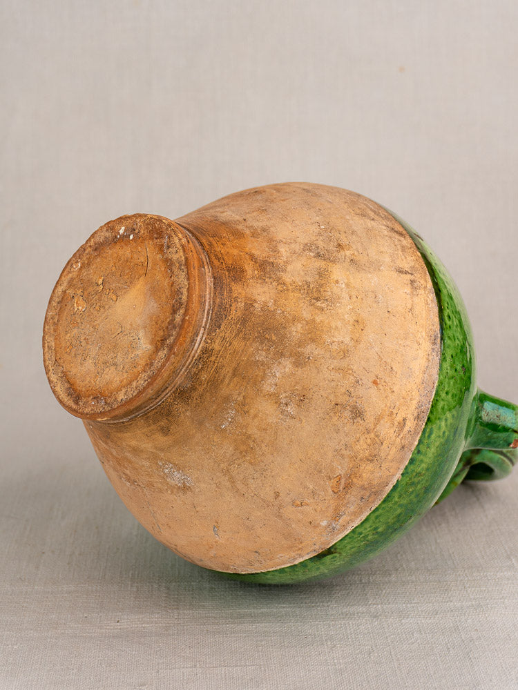 Antique French green glazed gargoulette cruche on its side, unglazed terracotta base visible, neutral background.
