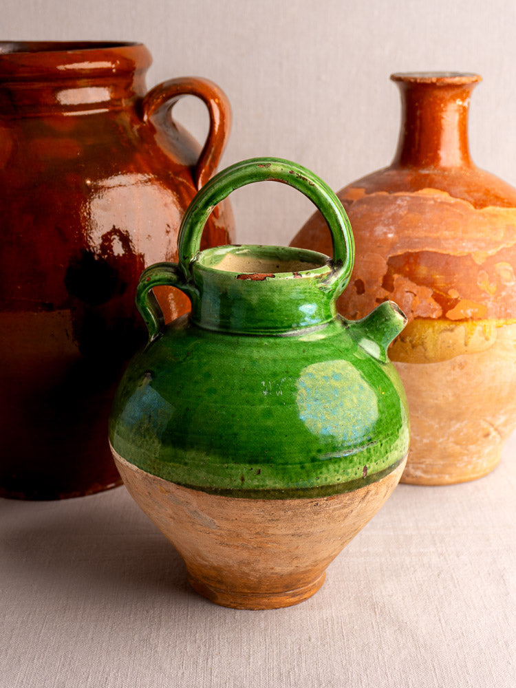 Antique French gargoulette with green-glazed upper terracotta and brown clay base on neutral fabric background.