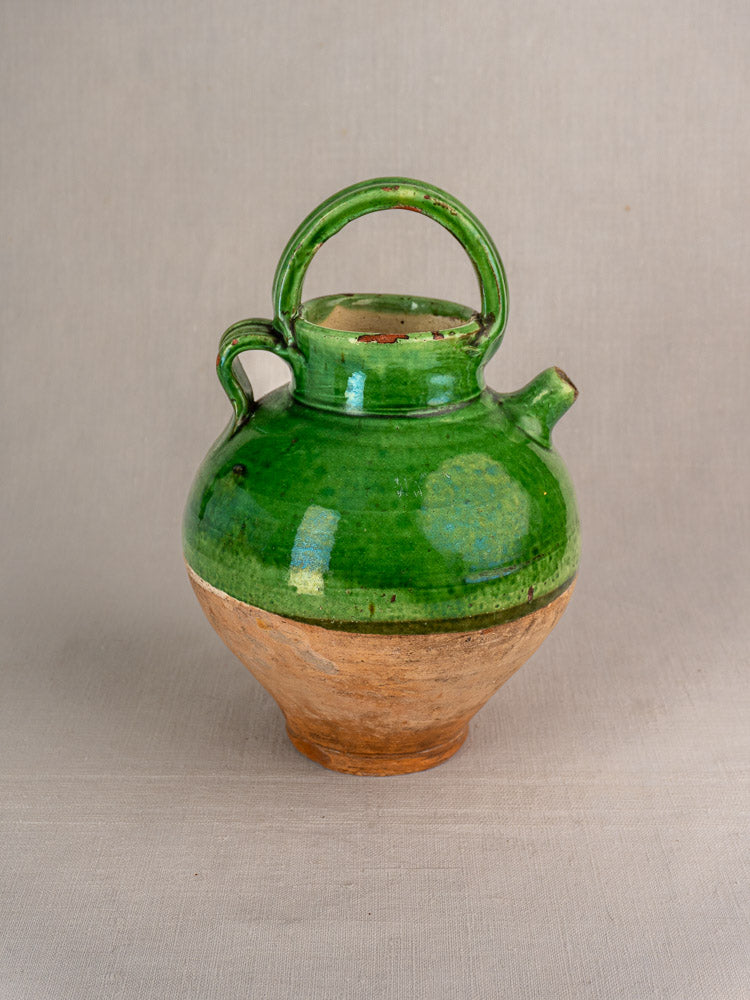 Antique French gargoulette with green-glazed upper terracotta and brown clay base on neutral fabric background.