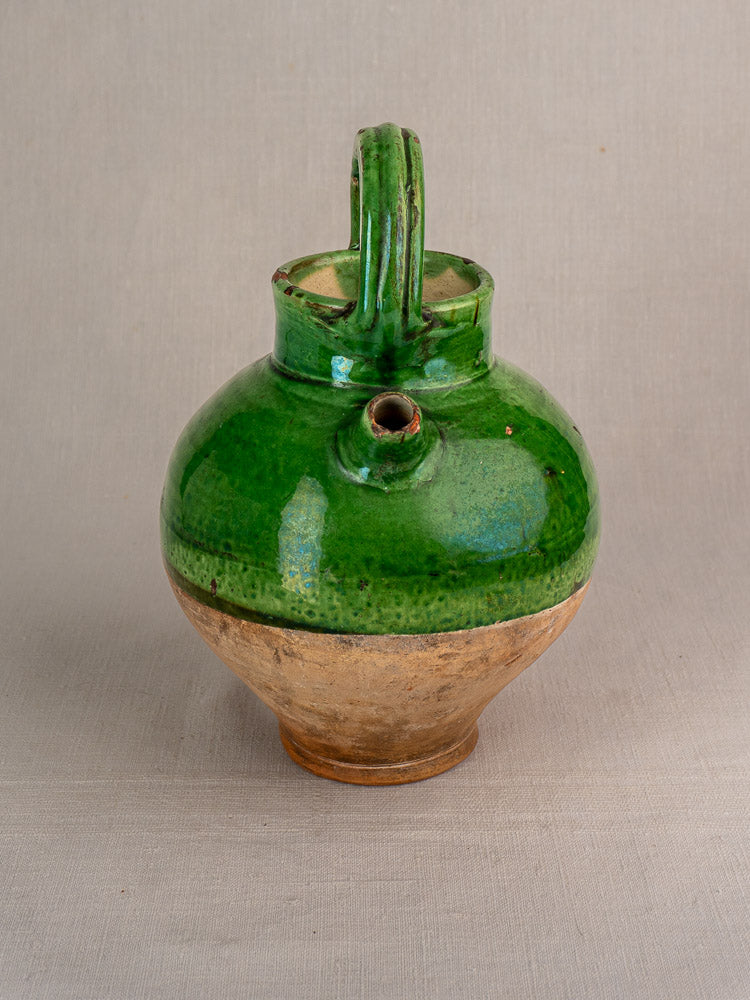 Antique French terracotta gargoulette water cruche with tan base, green glazed top, Provençal style, on light background.